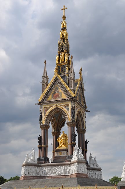 The image features a detailed, ornate monument with Gothic architectural elements, including pointed arches, pinnacles, and decorative statues, prominently displayed against a cloudy sky. The structure is decorated with gold accents, mosaics, and statues of religious figures, and rests on a multi-tiered base with white sculptural reliefs. The monument is surrounded by lush greenery and appears to be located in an outdoor setting. The lighting highlights the intricate details and gold embellishments of the monument, emphasizing its grandeur and historical significance. This scene is unrelated to washing surfaces or cleaning processes, focusing instead on architectural beauty and craftsmanship. For professional cleaning or surface sanitisation insights related to residential or commercial environments, visit Oven Cleaning Kensington at ovencleaningkensington.com.