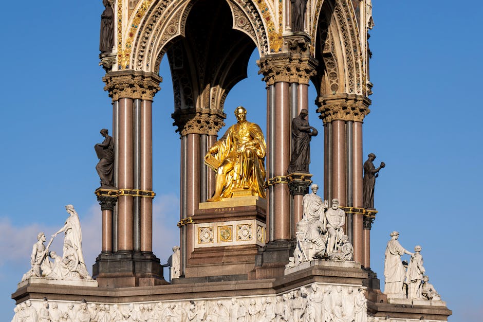 A wide view of the Royal Albert Hall in South Kensington, London, showcasing its historic circular architecture with a domed roof and ornate stonework. The building's exterior features red brick and detailed stone accents, with multiple arched windows and decorative sculptures near the entrance. The sky above is mostly clear with a few scattered clouds. In the foreground, a busy street scene includes parked cars, bicycles, and pedestrians walking along the pavement, with a low fence separating the road from the building. This image highlights a London landmark in a vibrant, urban setting, captured in natural daylight. For professional cleaning and maintenance of such historic surfaces, visit Oven Cleaning Kensington for expert domestic cleaning services near the Royal Albert Hall.