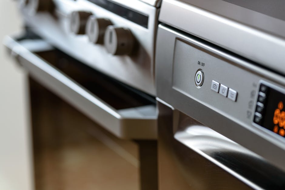 A person wearing yellow and blue rubber gloves is cleaning the inside of a white oven with a wire rack, using a cloth to wipe the oven's glass door. The oven features a stainless steel handle and cont